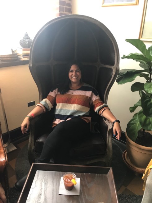author sitting in a wide covered chair with left leg crossed over right and arms over armrests.